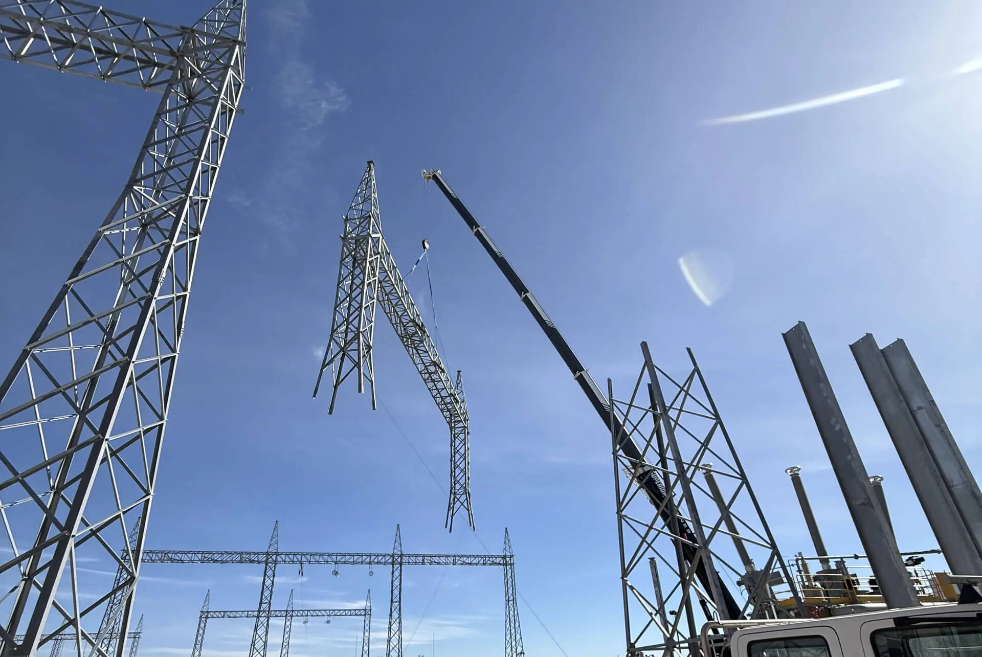 A crane lifts a large metal power transmission tower section into place at a construction site under a clear blue sky, with other tower structures nearby, as ecological consultants Australia ensure minimal environmental impact.